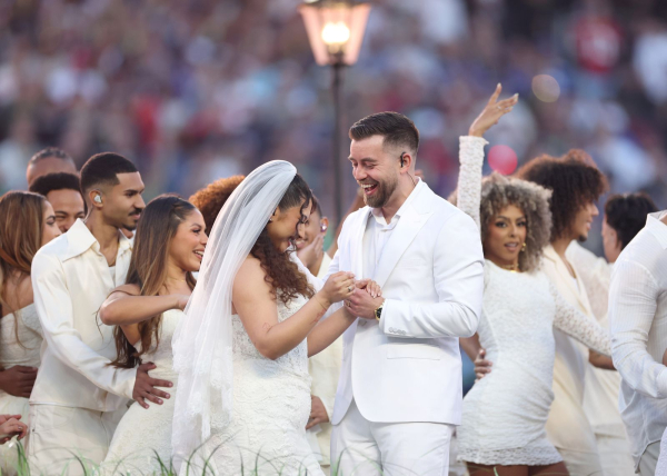 A couple gets married at the Super Bowl with dancers in white in the background